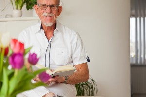 Senior man with glasses reading book in living room.